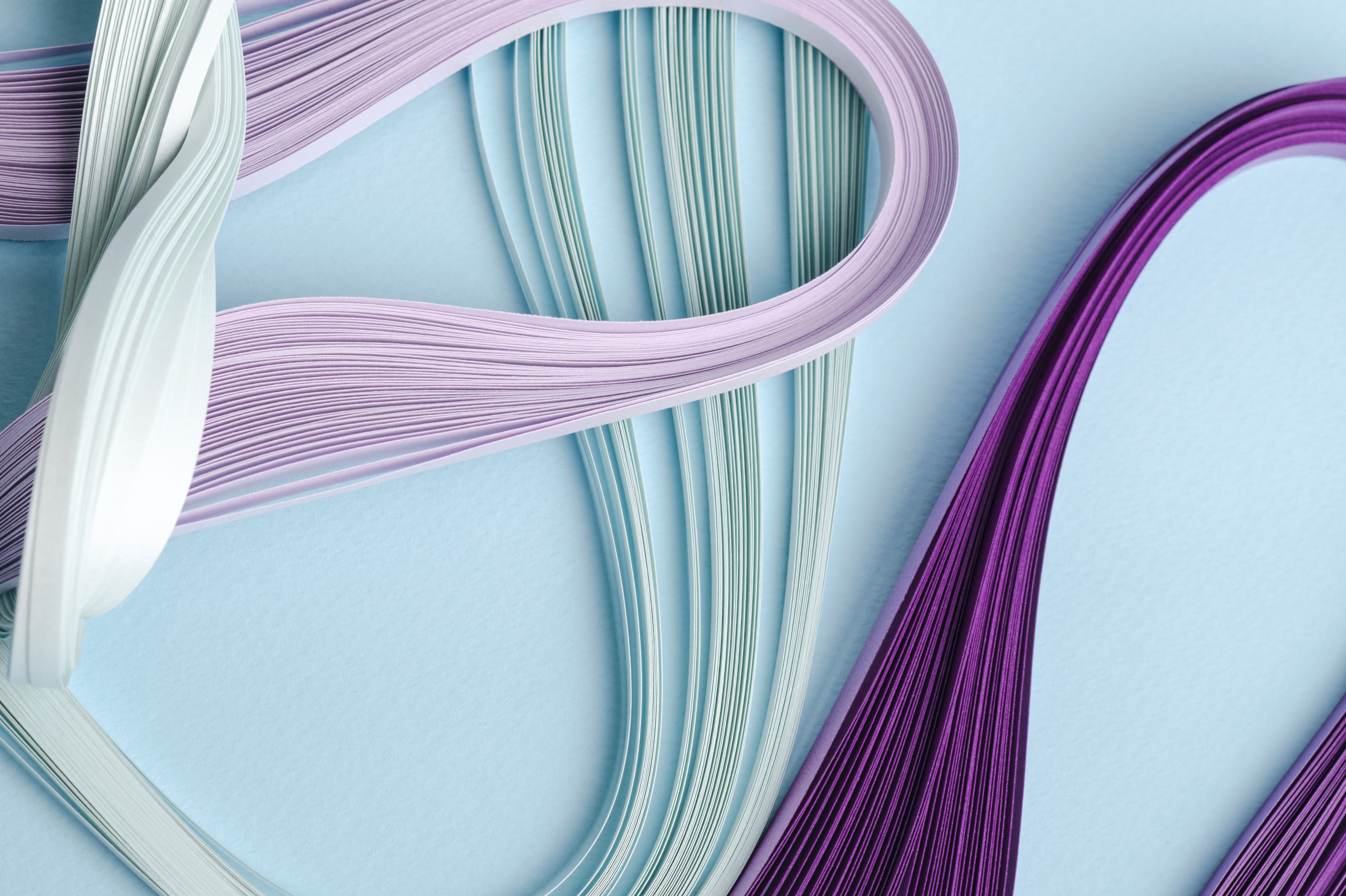 GKP_1255-1WEB Thin, wavy strips of lavender, mint green, and purple paper artfully arranged on a light blue background.