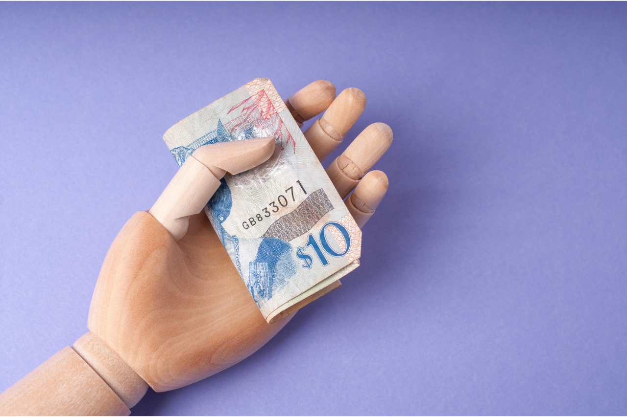 FLIP A wooden mannequin hand holds a folded ten-dollar bill against a purple background.