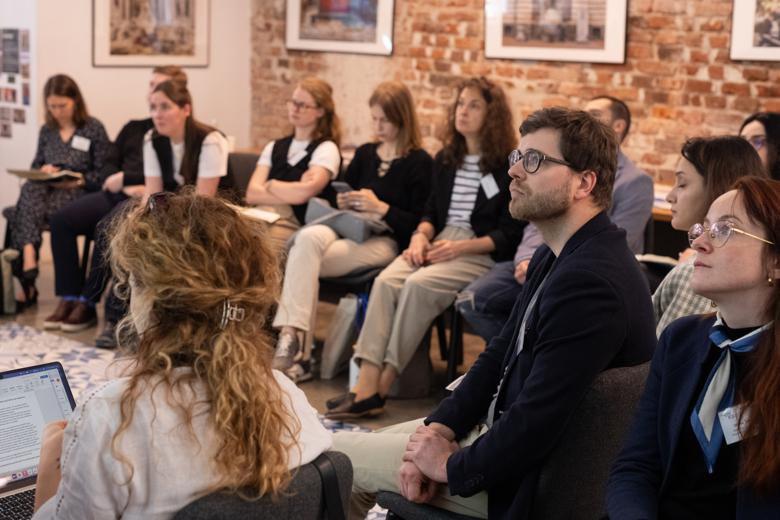 Sofia NECE Lab 2024 A group of people attentively listening in a seminar room with brick walls and framed art during Sofia NECE Lab 2024.