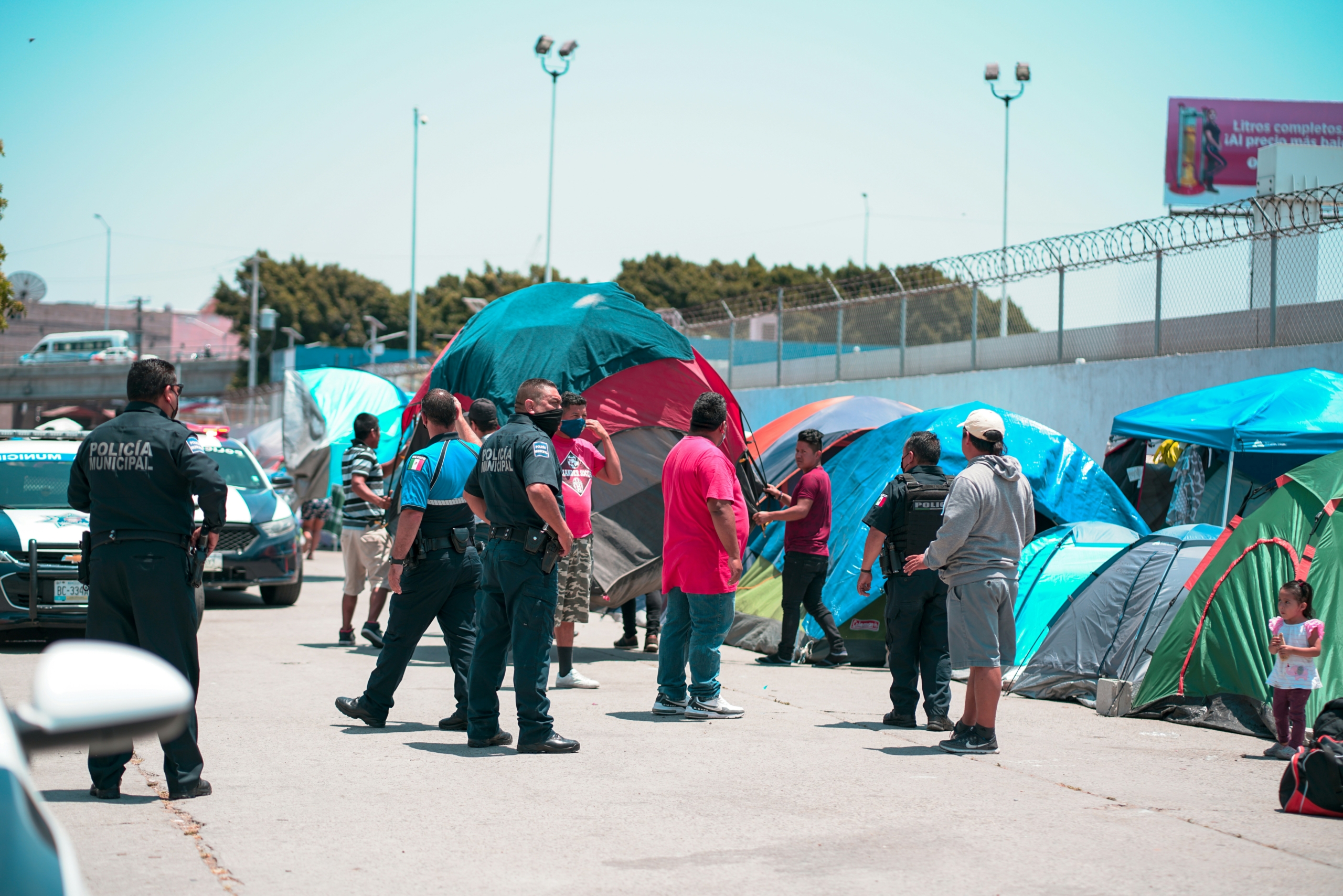 barbara-zandoval-AFWTg-5i7OY-unsplash Police officers and people gather near tents on a street. The setting conveys a tone of concern and engagement, with a child standing nearby.