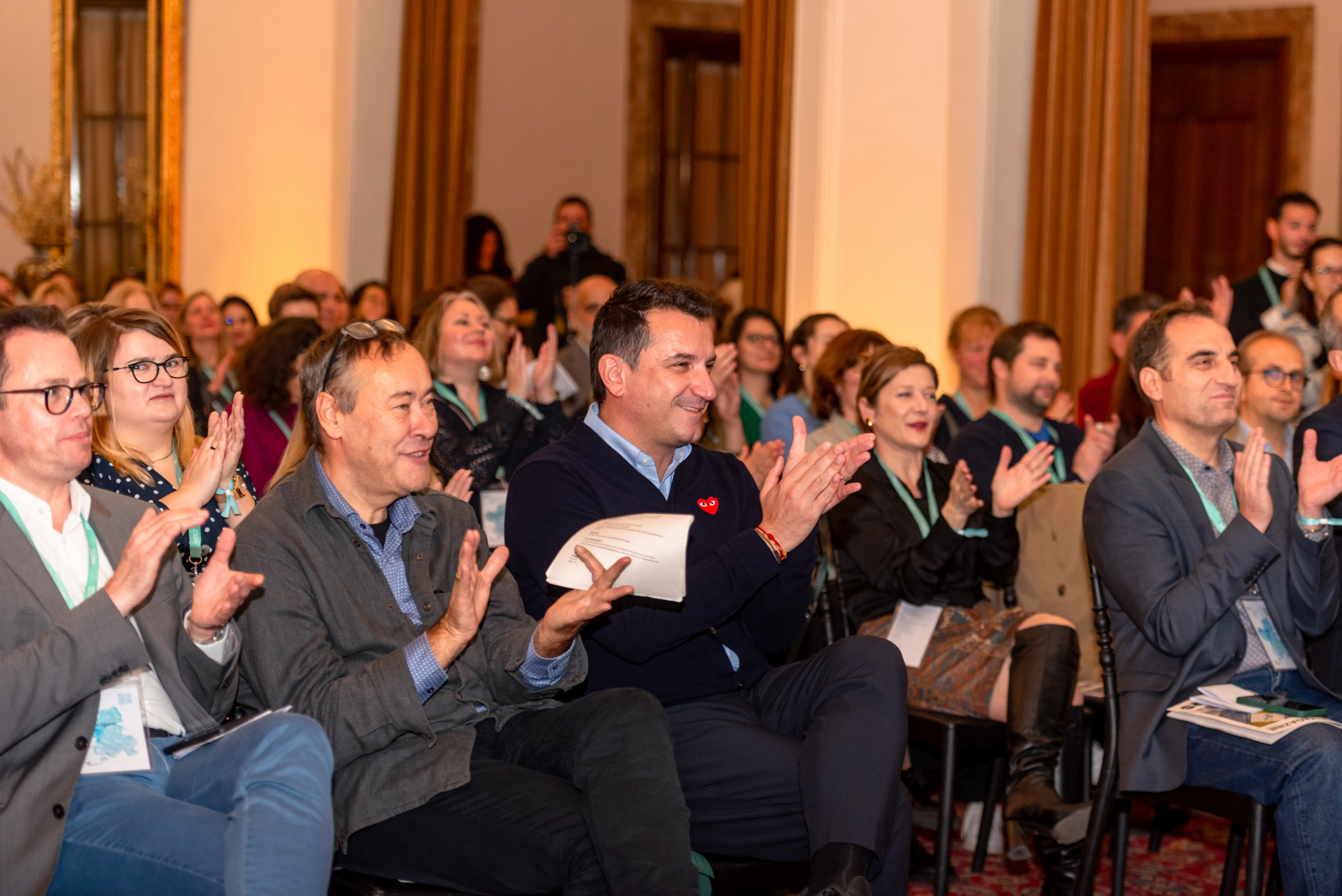 © THE CIVICS Innovation Hub | Geri Lula A diverse crowd of people seated indoors applauds enthusiastically, conveying a positive and engaging atmosphere at NECE Festival 2024.