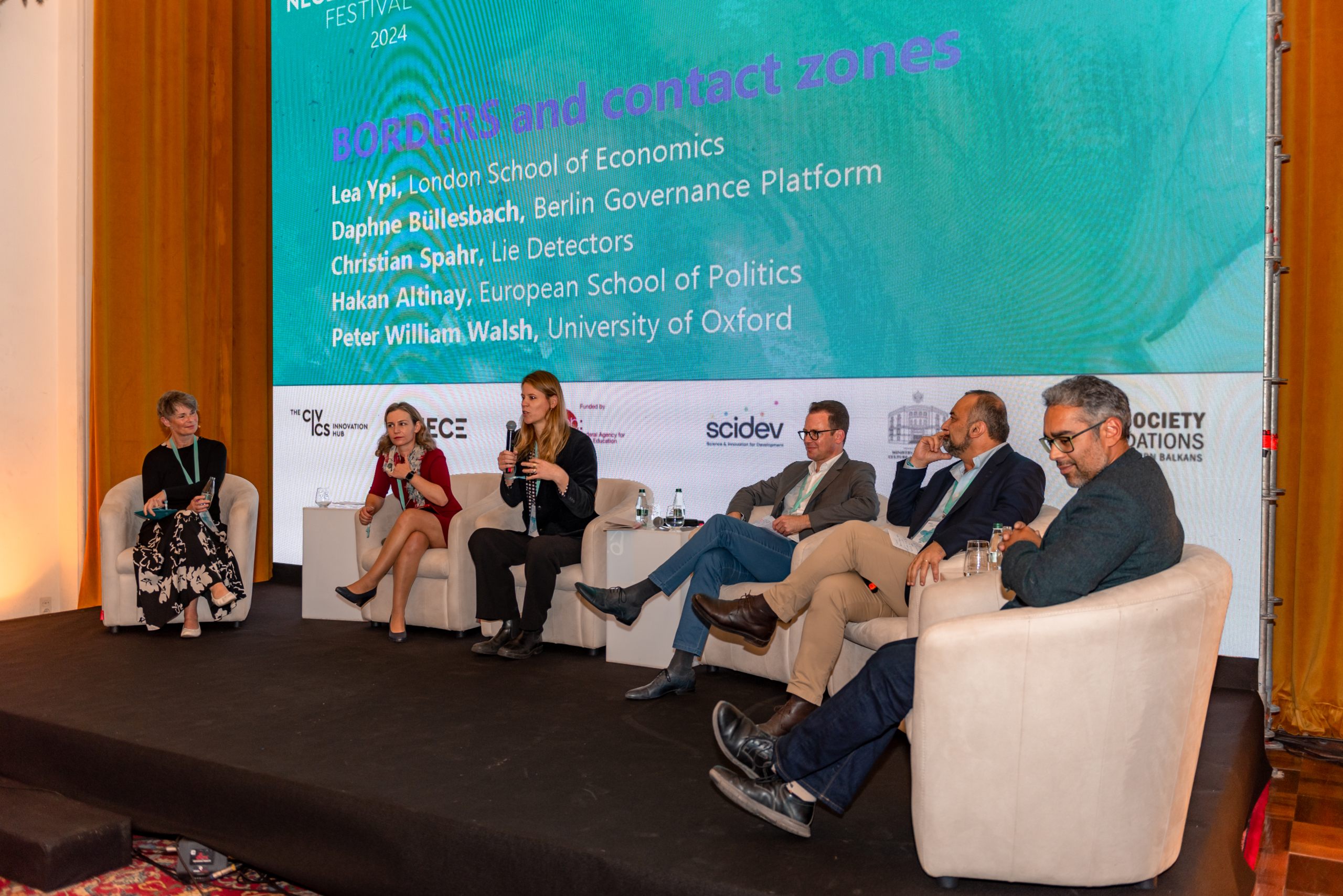 © THE CIVICS Innovation Hub | Geri Lula A panel of six people sit on stage at NECE Festival 2024. A large screen behind them displays the title “BORDERS and contact zones.”