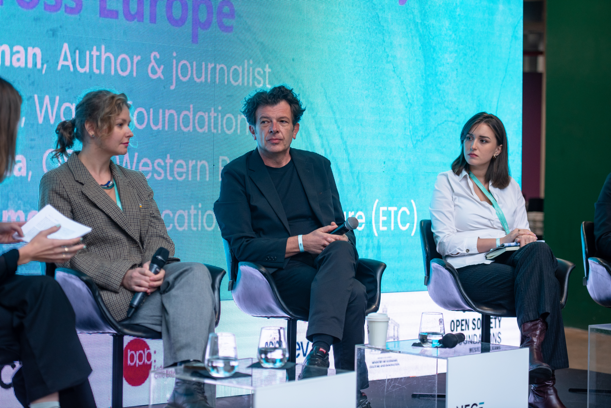 © THE CIVICS Innovation Hub | Geri Lula Three people on a panel discussion on stage during NECE Festival 2024. Two women and one man sit in chairs, each holding a microphone.