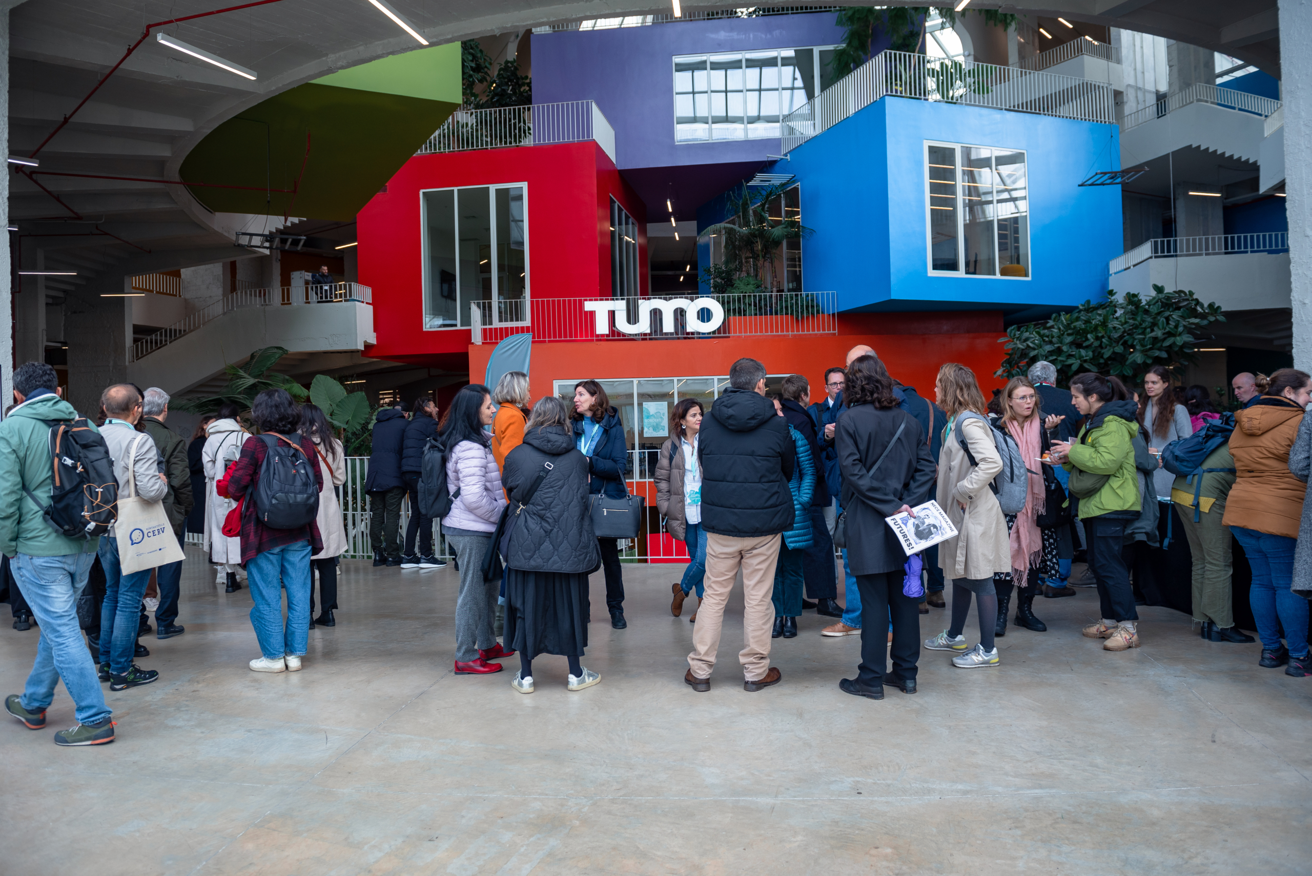 © THE CIVICS Innovation Hub | Geri Lula A group of people in winter clothing gather inside a modern building with colorful, geometric structures during NECE Festival 2024.