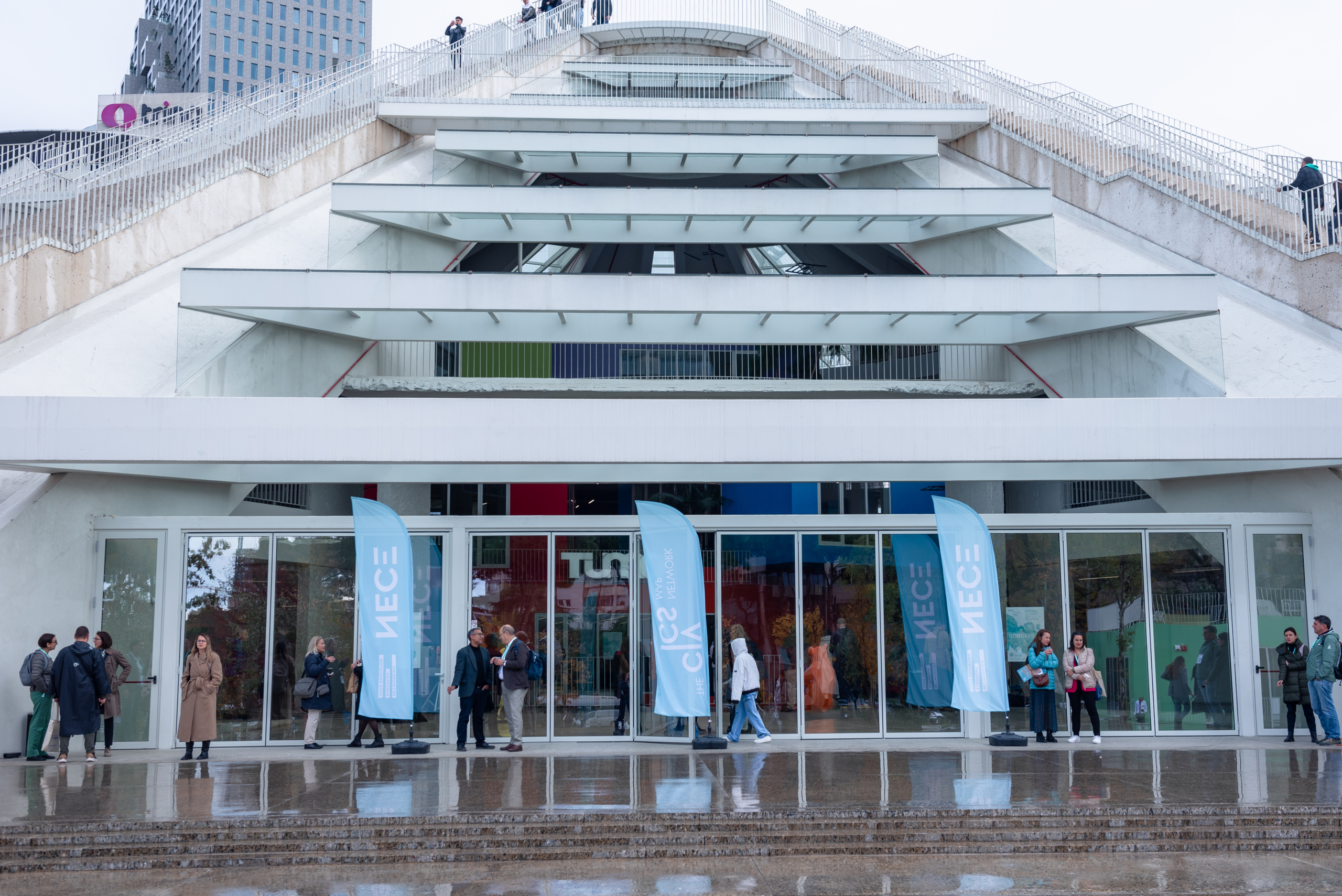 © THE CIVICS Innovation Hub | Geri Lula The Pyramid of Tirana entrance with glass doors and light blue flags marked "NECE."