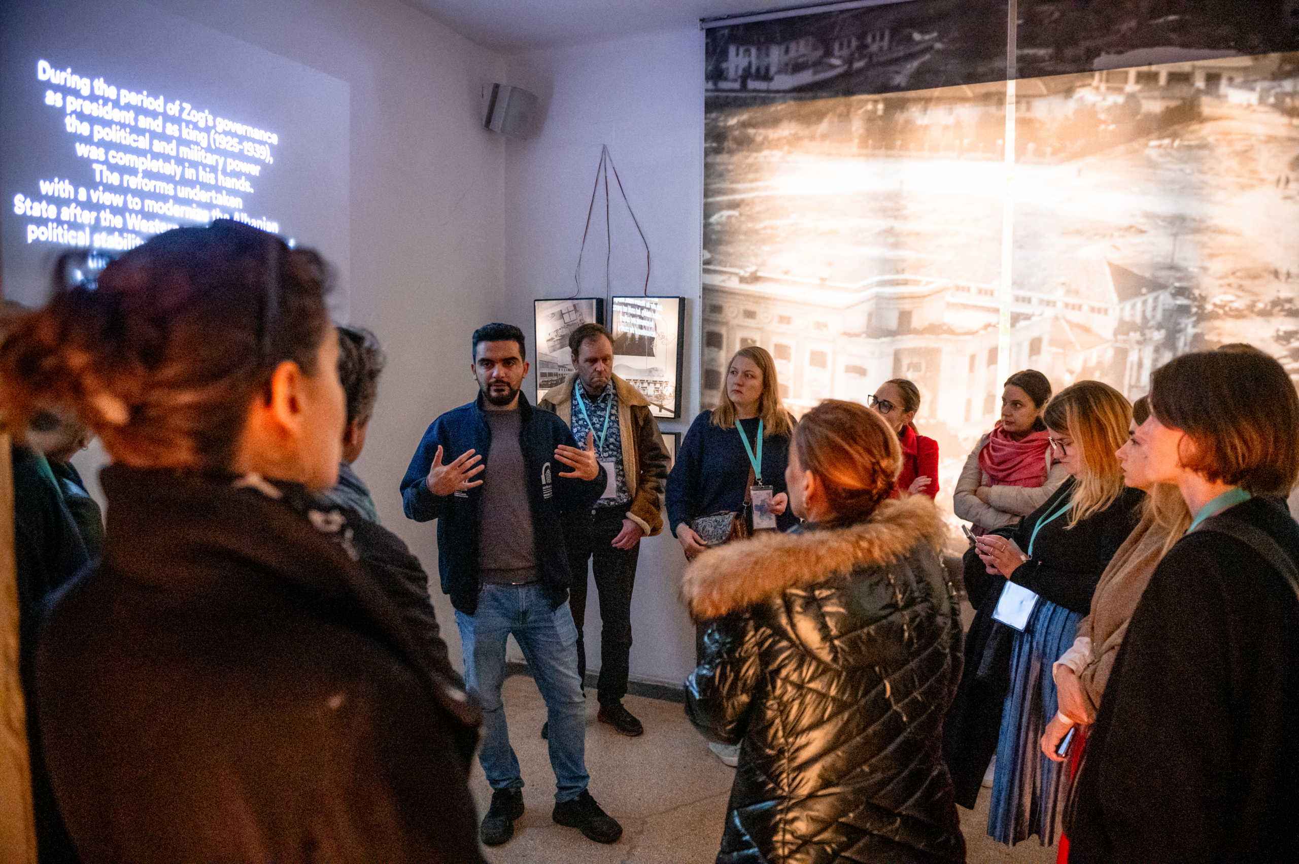 © THE CIVICS Innovation Hub | Geri Lula A man speaks to a group of engaged listeners in an indoor setting during NECE Festival 2024. The room features historical images and text on the walls,