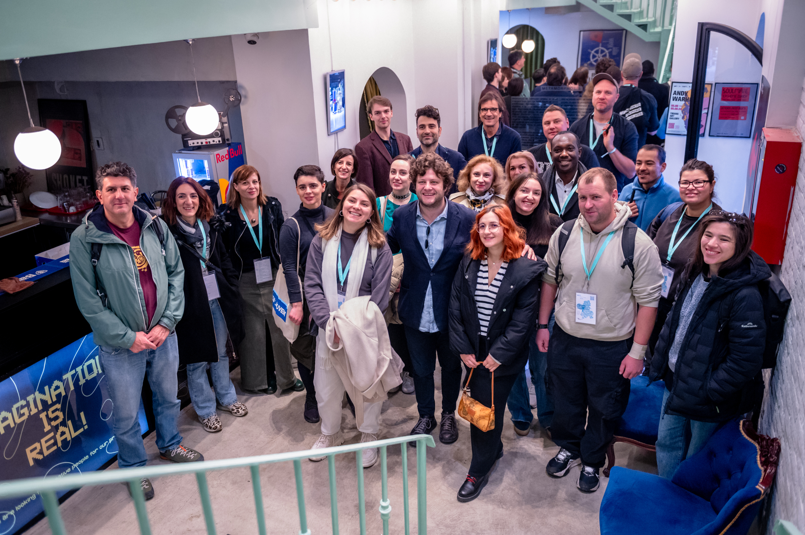 © THE CIVICS Innovation Hub | Geri Lula A diverse group of people smiling at the camera in a cozy, brightly lit indoor space.