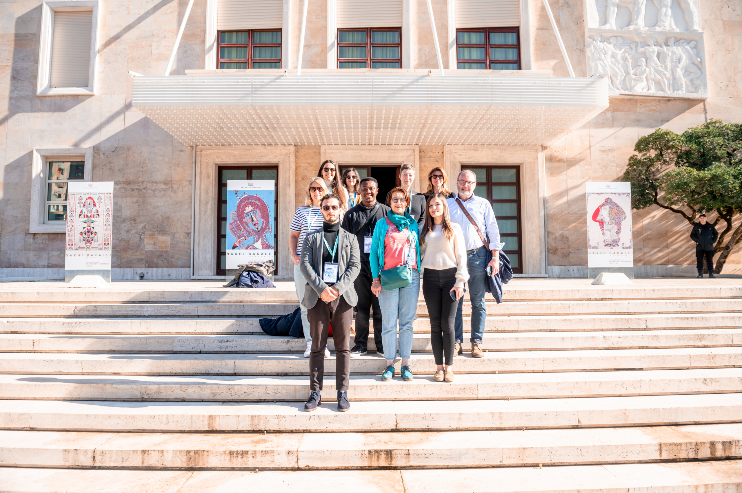 © THE CIVICS Innovation Hub | Geri Lula A group of ten people stands smiling on stone steps outside a building with large windows.