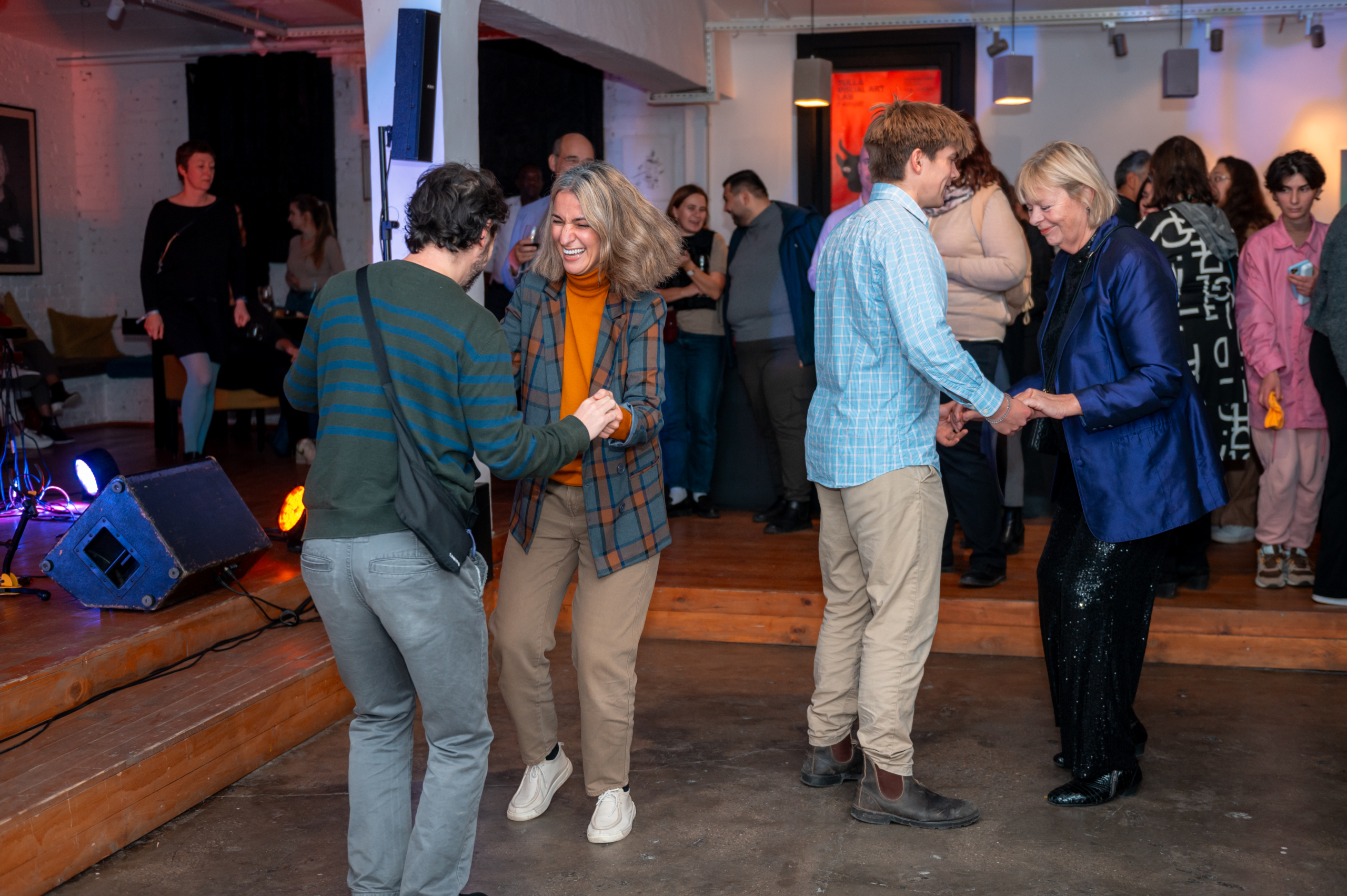 © THE CIVICS Innovation Hub | Geri Lula A lively indoor party scene with two pairs of people dancing during NECE Festival 2024. One woman in a plaid jacket smiles widely. Others chat and enjoy the vibrant atmosphere.