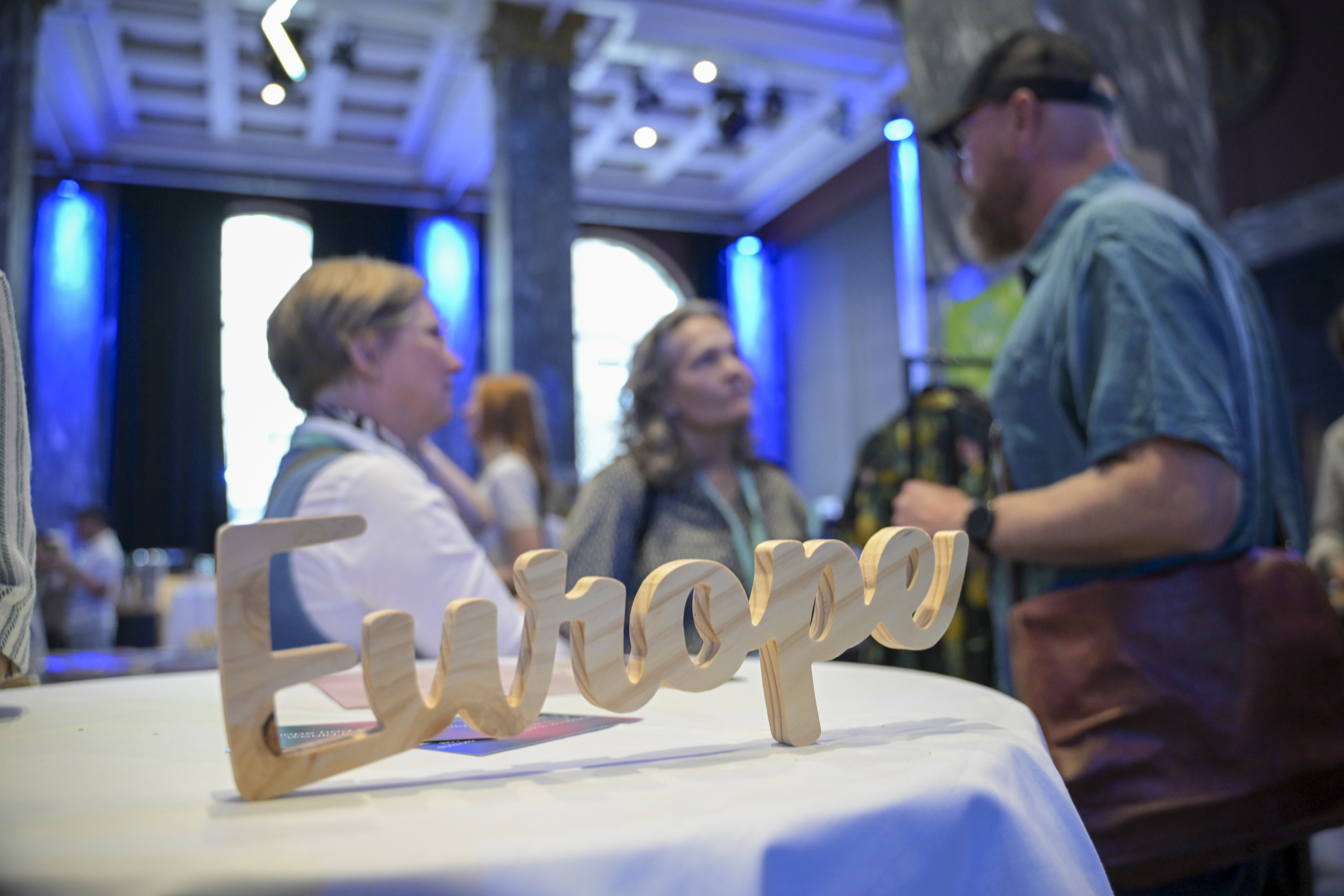 © THE CIVICS Innovation Hub / Werner Anderson A wooden "Europe" sign on a table in the foreground, with people in conversation at the NECE Festival: HOPE