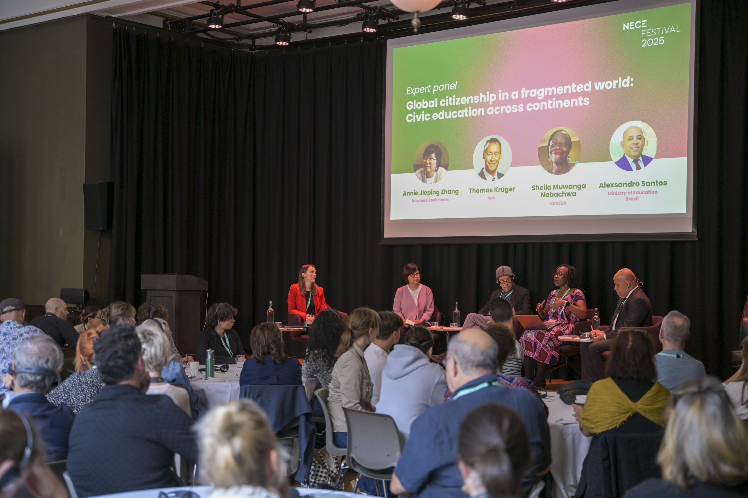 © THE CIVICS Innovation Hub / Werner Anderson An expert panel at NECE Festival 2025 discusses global citizenship and civic education. Five panelists sit on stage, engaging with an attentive audience.