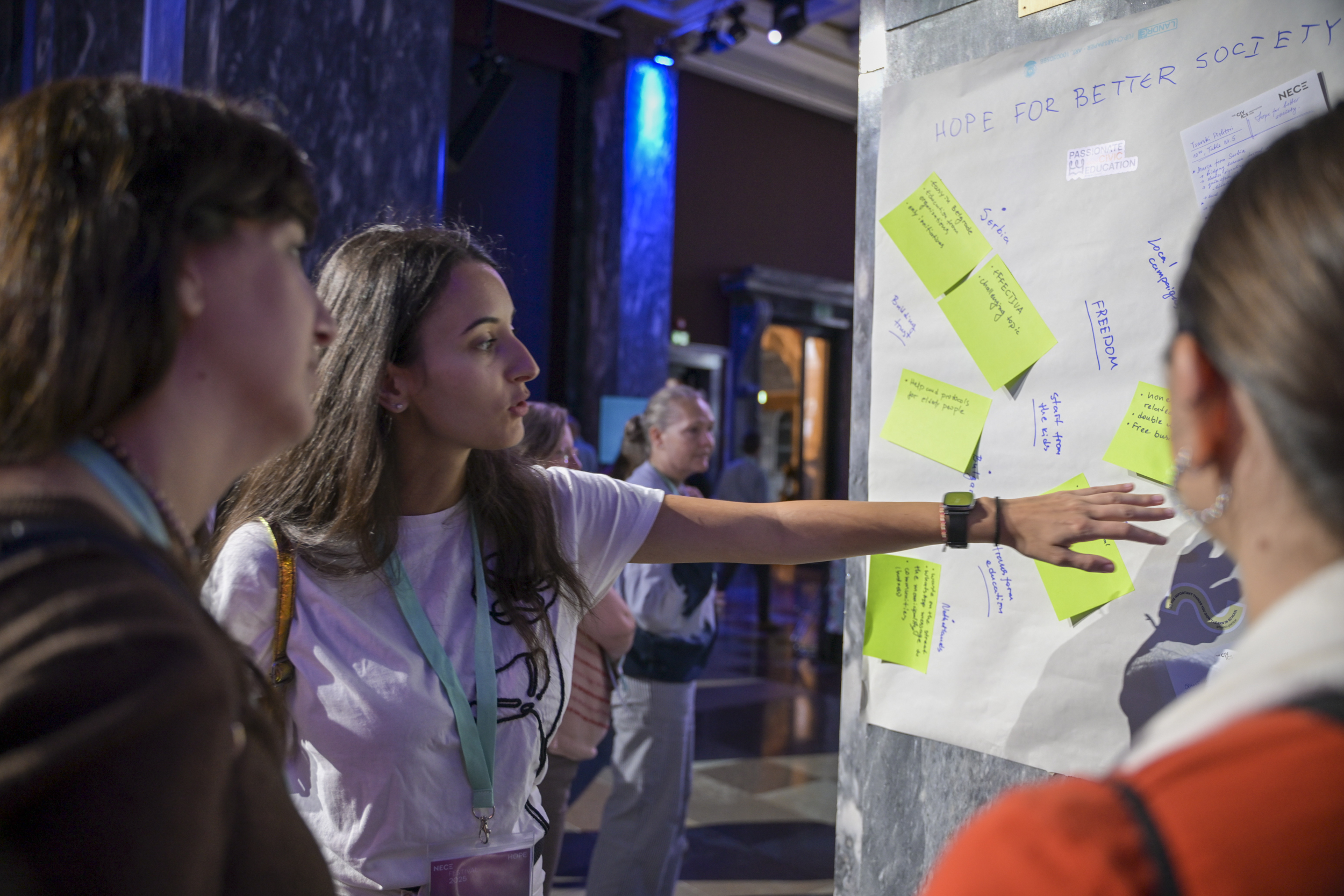 © THE CIVICS Innovation Hub / Werner Anderson A woman gestures towards a wall with notes and "Hope for Better Society" written on it at the NECE Festival: HOPE.