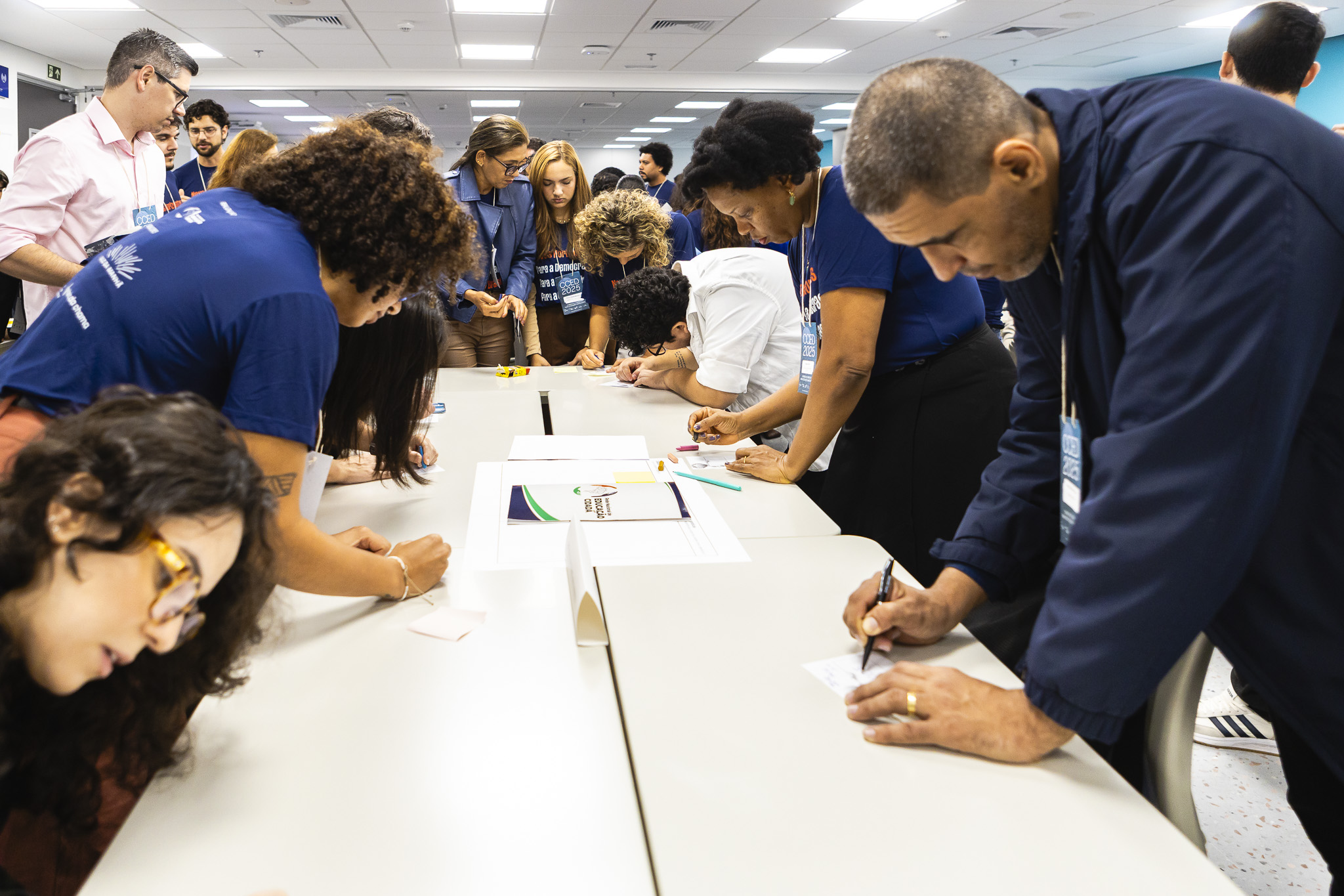 ©RedeNEC The photo shows participants of the event, standing around a table, writing notes on small papers.