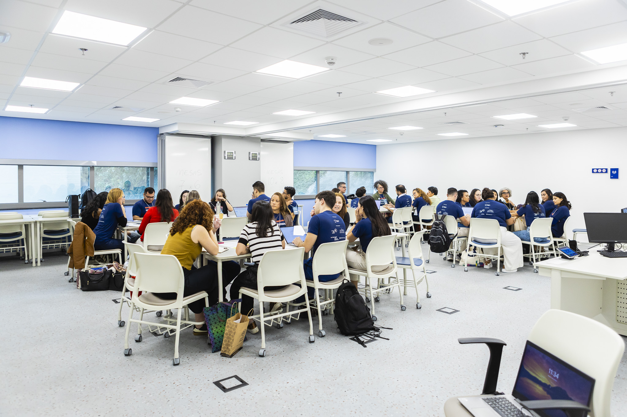 ©RedeNec The photo shows a room, where different groupes of people are sitting on tables and work together.
